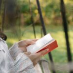 kobieta siedząca z książką na ławce w ogrodzie